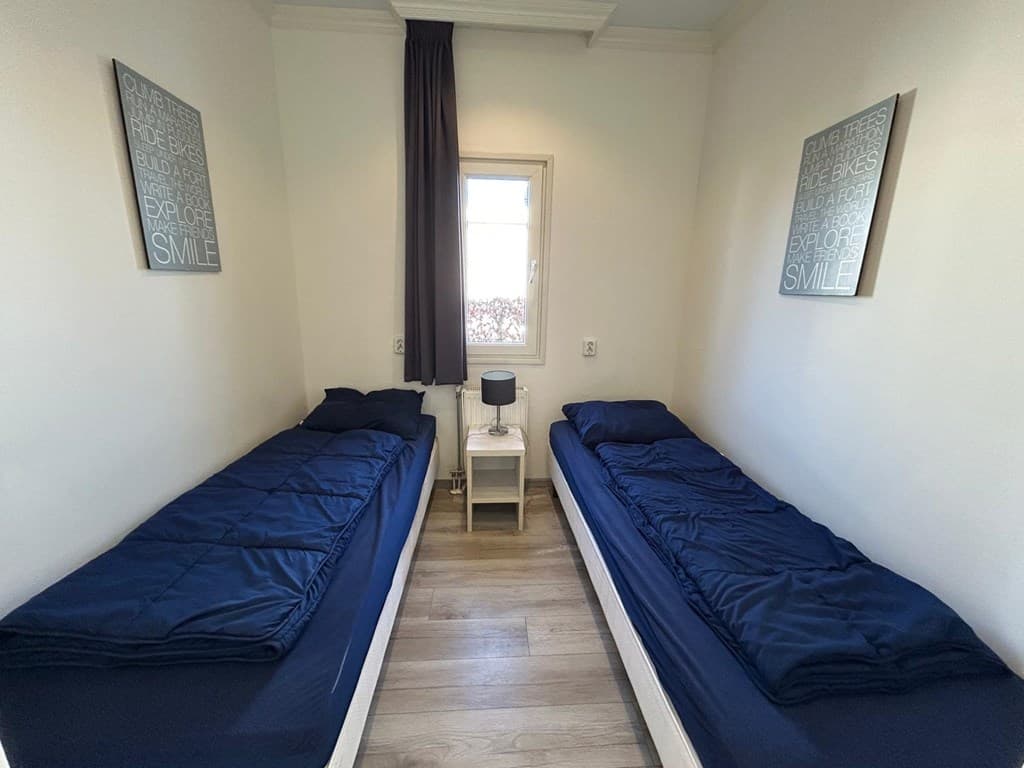 Slaapkamer met twee eenpersoonsbedden, een nachtkastje en een raam met zicht naar buiten