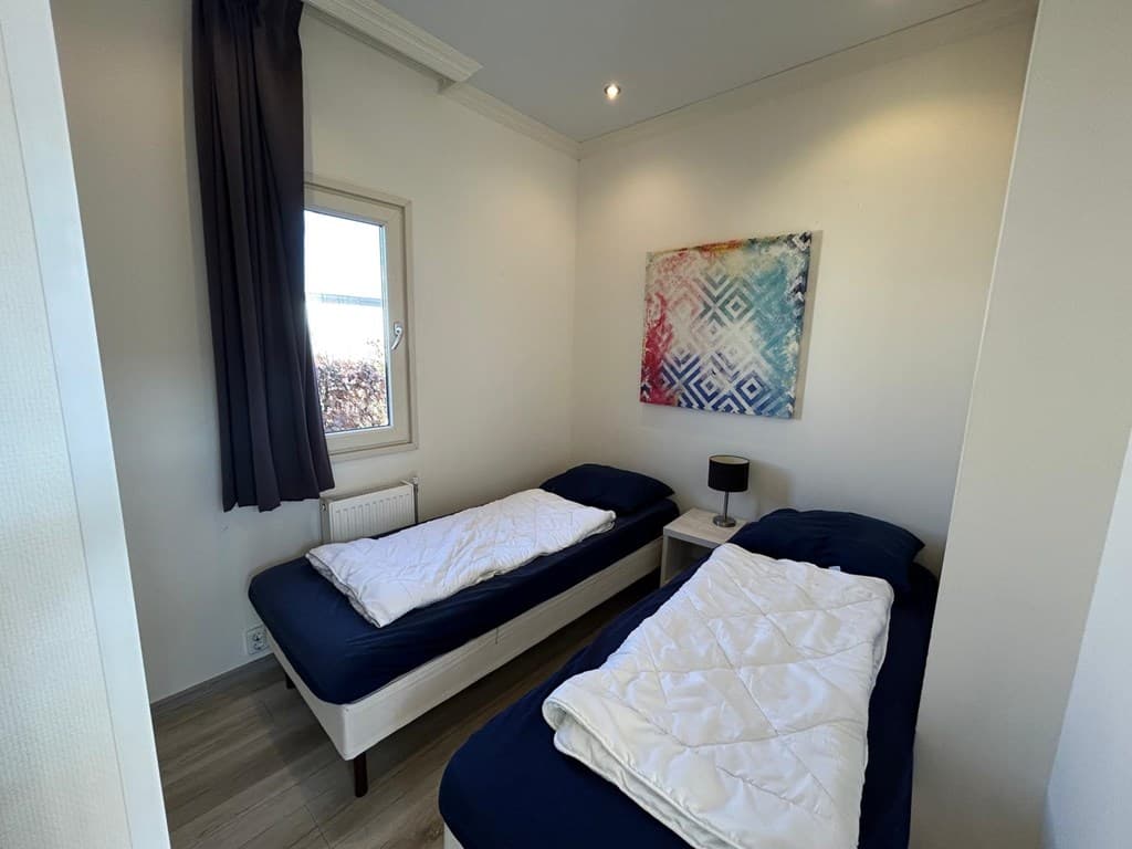 Slaapkamer met twee eenpersoonsbedden, nachtkastje en raam met uitzicht op buiten.