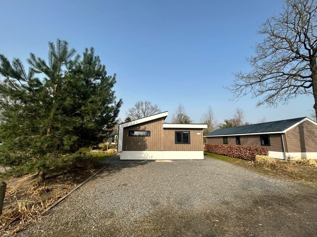 Moderne vakantiewoning met een houten gevel en moderne daklijn, omringd door een grindpad en groene bomen.