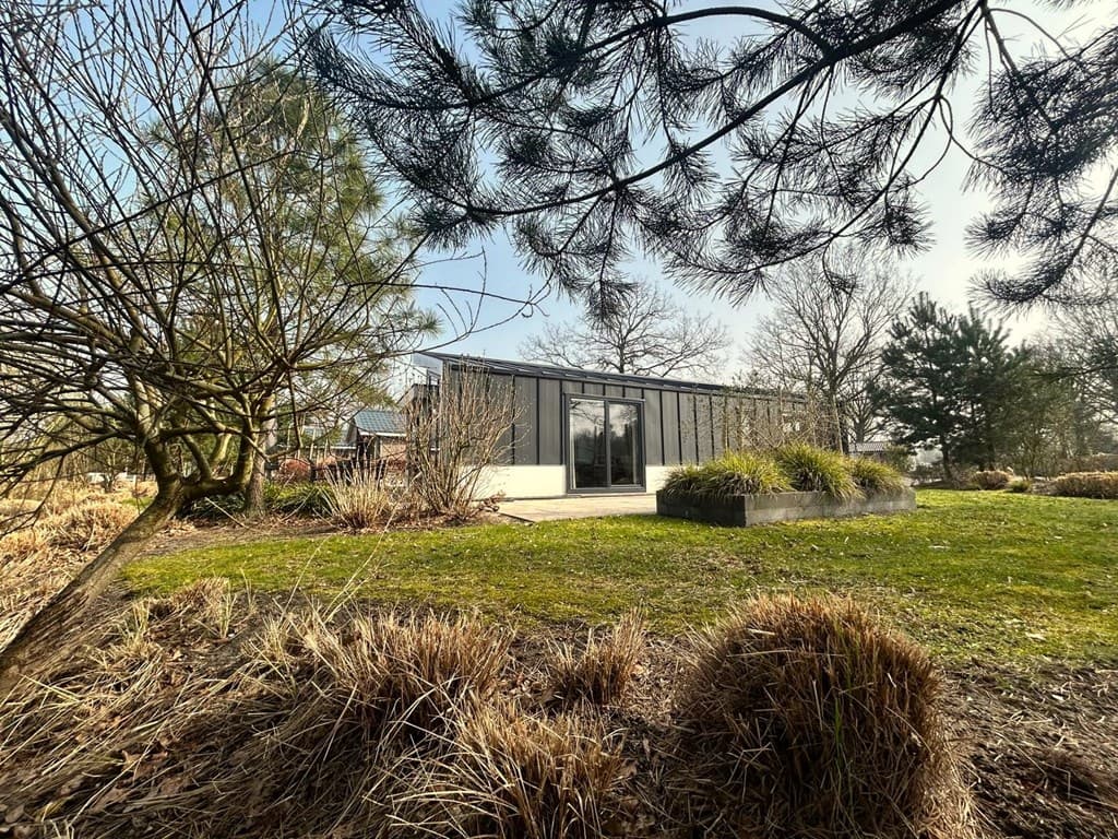 Moderne vakantiewoning omgeven door groen, met een grote tuin en grote ramen in de gevel.
