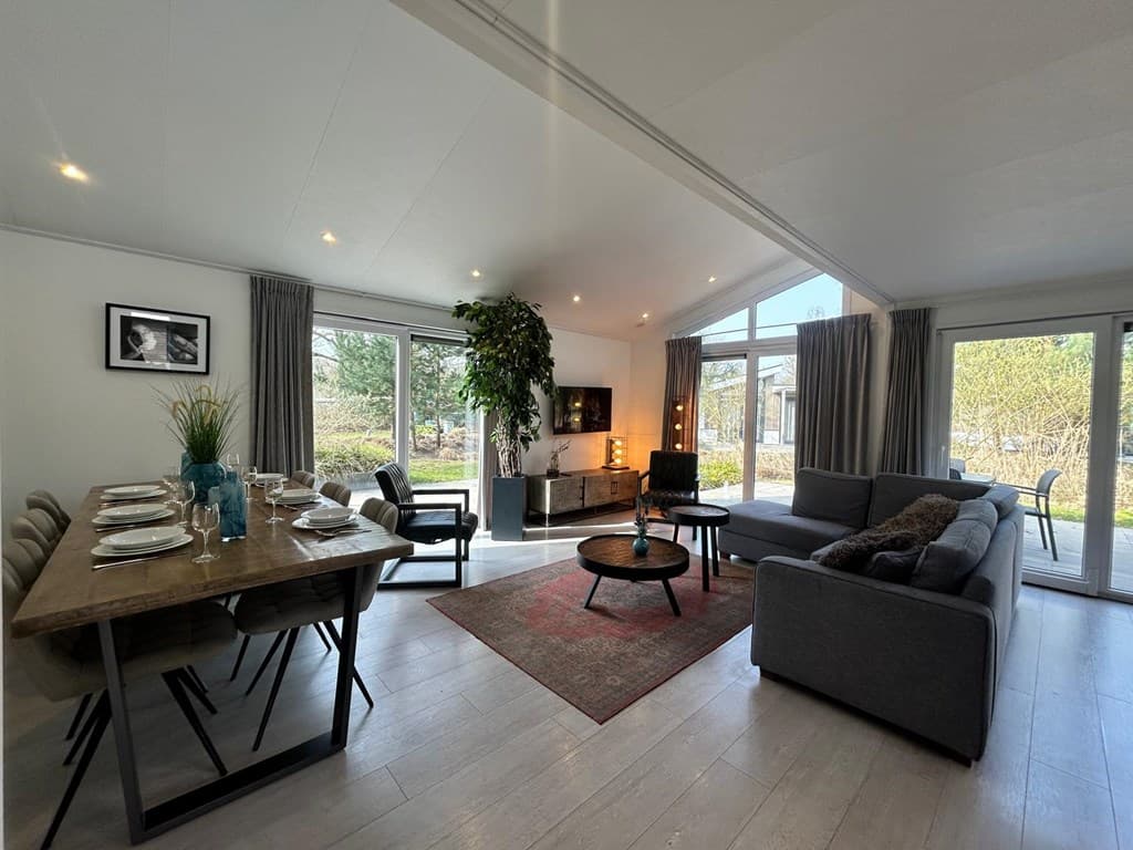 Moderne woonkamer met eettafel, zithoek, grote ramen en uitzicht op de tuin.
