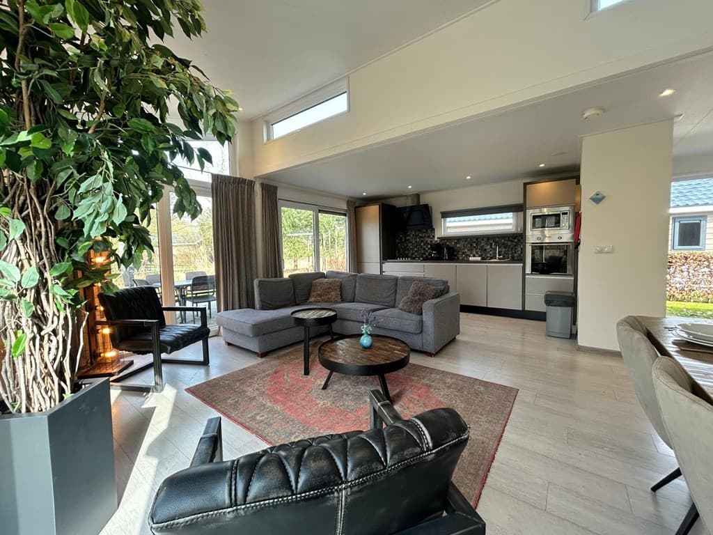 Moderne woonkamer met zitgedeelte, open keuken en grote ramen voor veel natuurlijk licht.