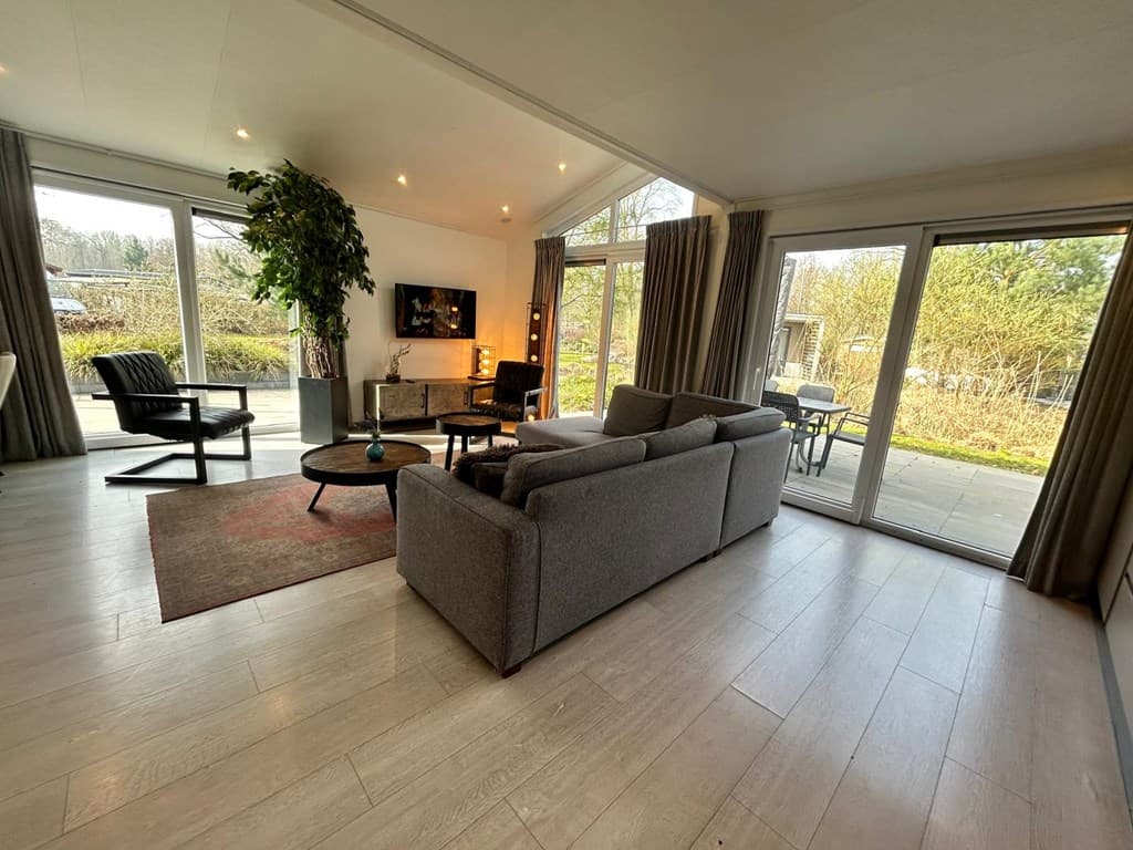 Woonkamer met ruime zithoek, grote ramen naar buiten en een modern interieur met een vloerkleed.
