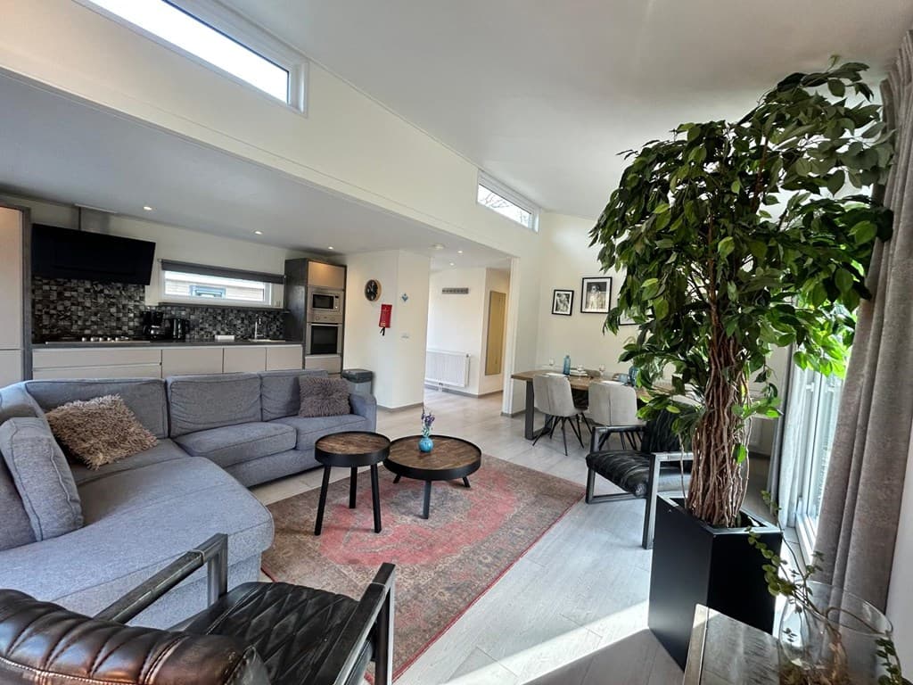 Moderne woonkamer met zithoek, eettafel en open keuken, grote ramen en groene planten in EuroParcs Zuiderzee