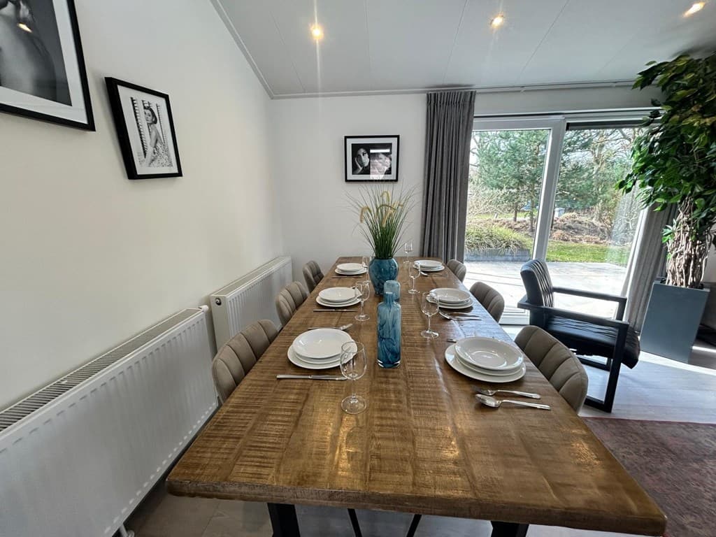 Eettafel met stoelen, gedekt met borden en glazen, naast een grote glazen deur met uitzicht op buiten.