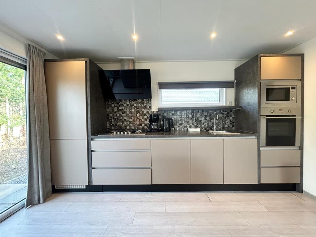 Moderne keuken met grijze kastjes, inbouwapparatuur en een raam met uitzicht op de buitenruimte.