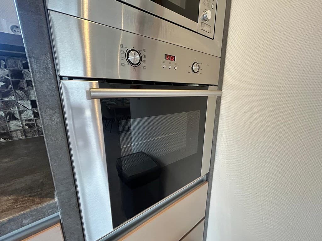 Ingebouwde oven en magnetron in moderne keuken met een schimmige achterwand en een prullenbakje zichtbaar.