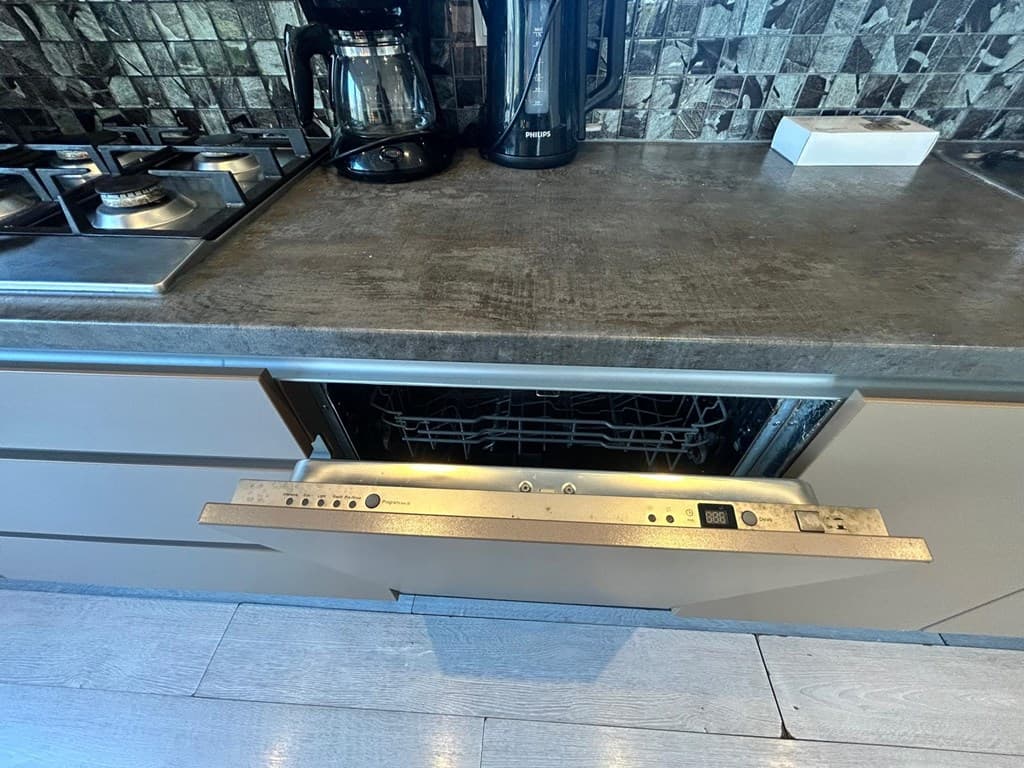 Inbouwvaatwasser met open lade in moderne keuken met een stenen werkblad en koffiezetapparaat achterop.