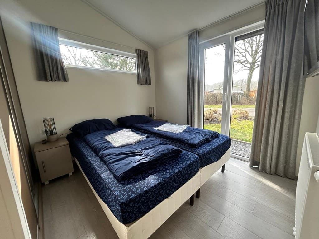 Slaapkamer met twee eenpersoonsbedden, raam met uitzicht op de tuin en een nachtkastje naast het bed