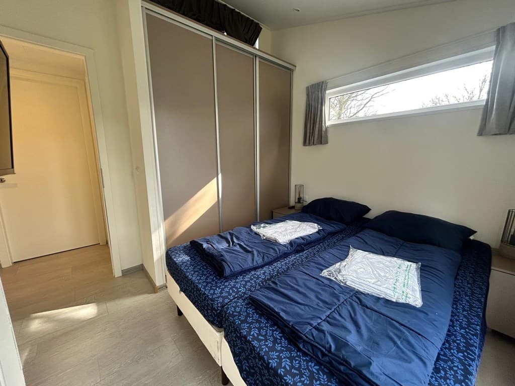 Slaapkamer met twee eenpersoonsbedden, kastwand, en raam met natuurlijk lichtinval.