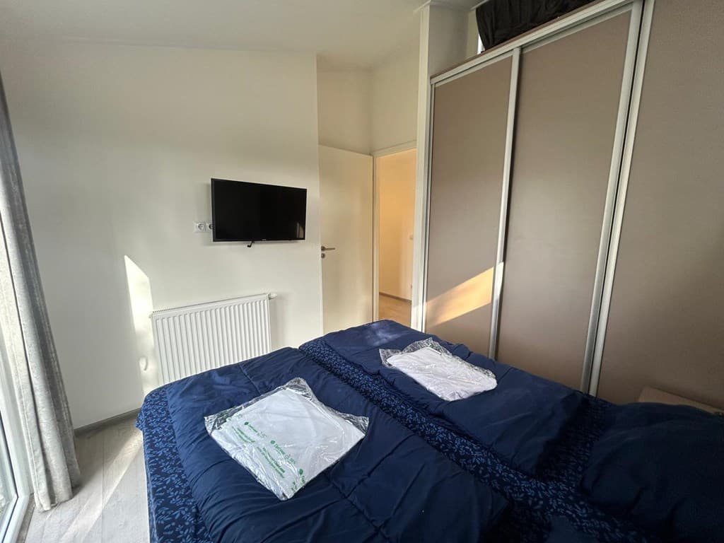 Slaapkamer met een tweepersoonsbed, televisie en inbouwkast, met een raam dat natuurlijk licht binnenlaat.