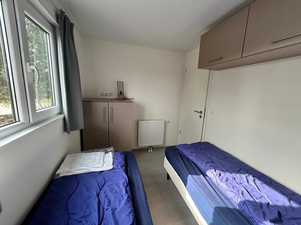 Slaapkamer met twee eenpersoonsbedden en een kast, ramen met gordijnen en een verwarmingselement