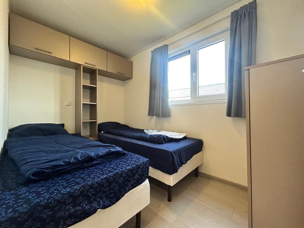 Slaapkamer met twee eenpersoonsbedden, kast en raam met gordijnen in EuroParcs Zuiderzee