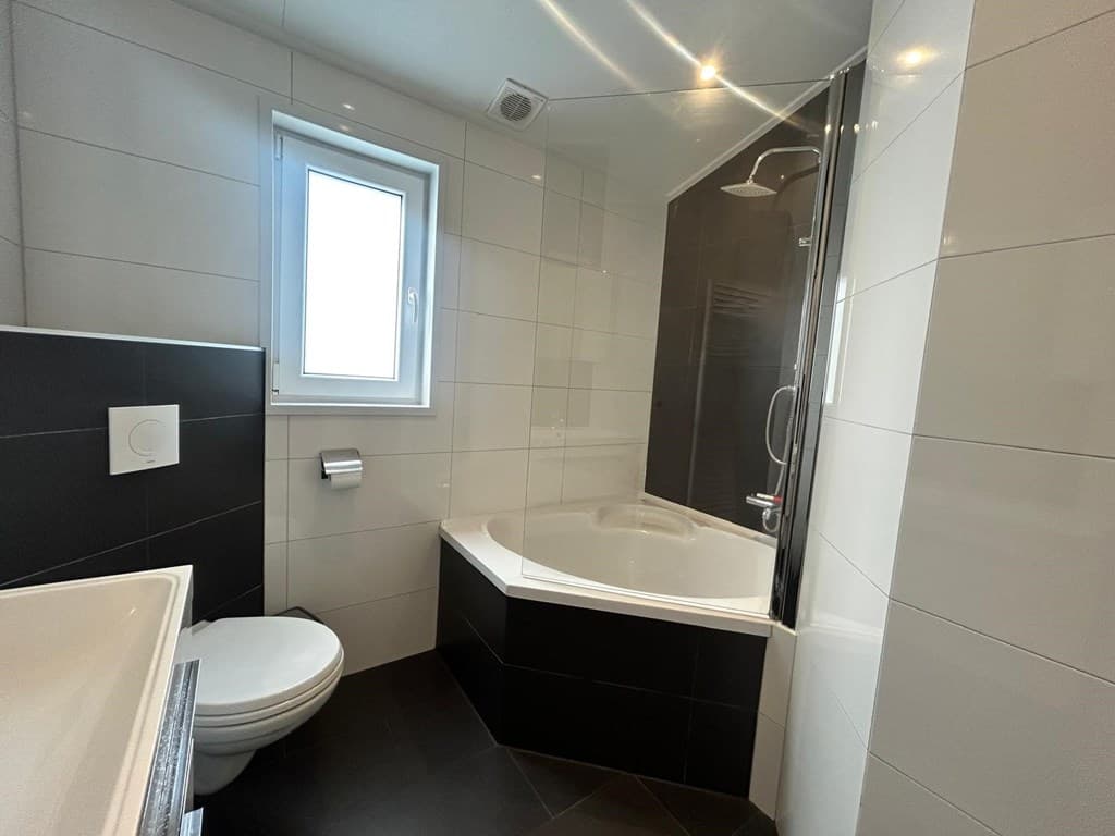 Moderne badkamer met bad, douche, toilet en raam, betegeld met witte en zwarte tegels