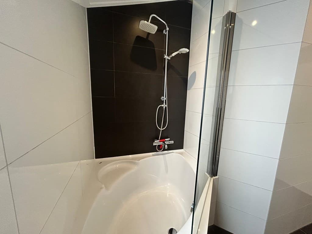 Badkamer met een ligbad, inloopdouche en moderne wandtegels in zwart en wit.