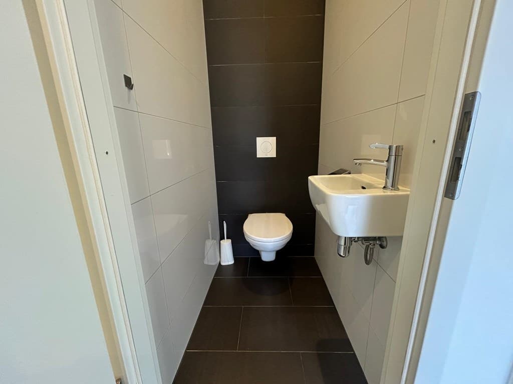 Modern toilet met zwart-witte tegels, een wandtoilet en een kleine wastafel met kraan aan de muur.