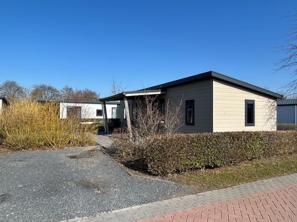 Buitenzijde van een vakantiewoning met tuinen en een bestrate oprit onder een blauwe lucht