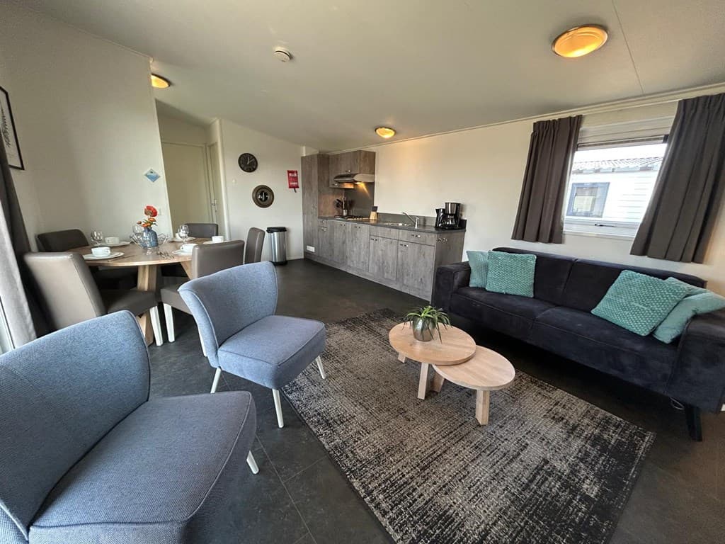 Moderne woonkamer met zithoek, eettafel en open keuken, voorzien van donkere en lichte elementen en raam met natuurlijk licht