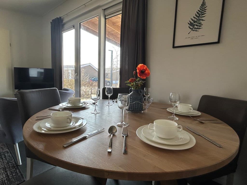Eettafel met vier gedekte plaatsen, bloemenvaas en uitzicht op de buitenruimte door de raampartij