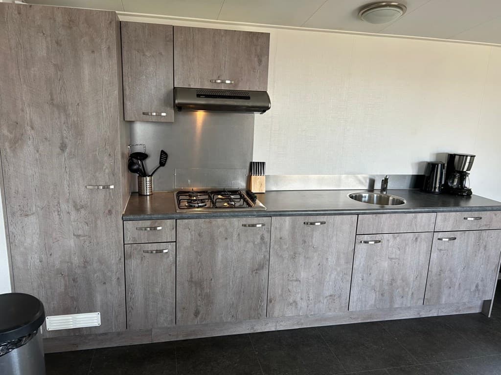 Keuken met moderne kastjes, kookplaat, afzuigkap, gootsteen en koffiezetapparaat in EuroParcs Markermeer.