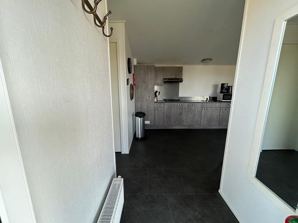 Open keuken met moderne apparatuur en zicht op entree, afgewerkt met een donkere tegelvloer.