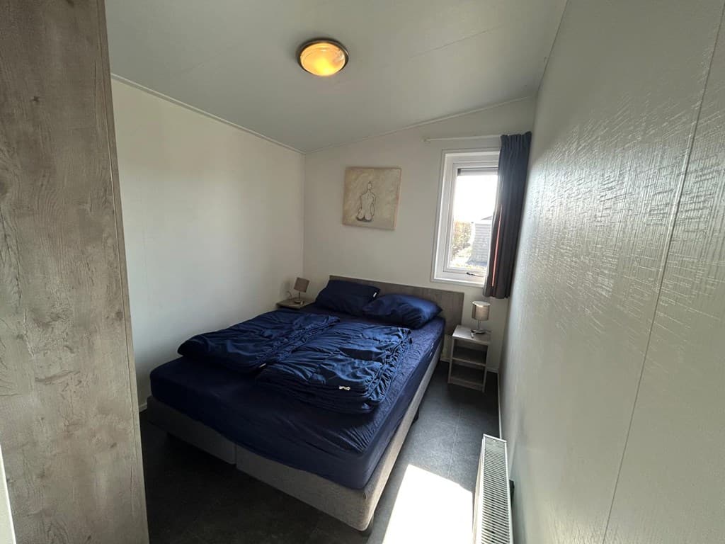 Sfeervolle slaapkamer met een tweepersoonsbed, nachtkastjes en raam met zicht naar buiten.