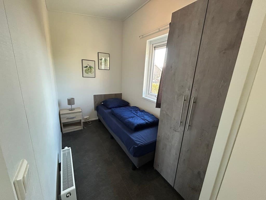 Slaapkamer met een eenpersoonsbed, nachtkastje, kledingkast en raam met uitzicht naar buiten.