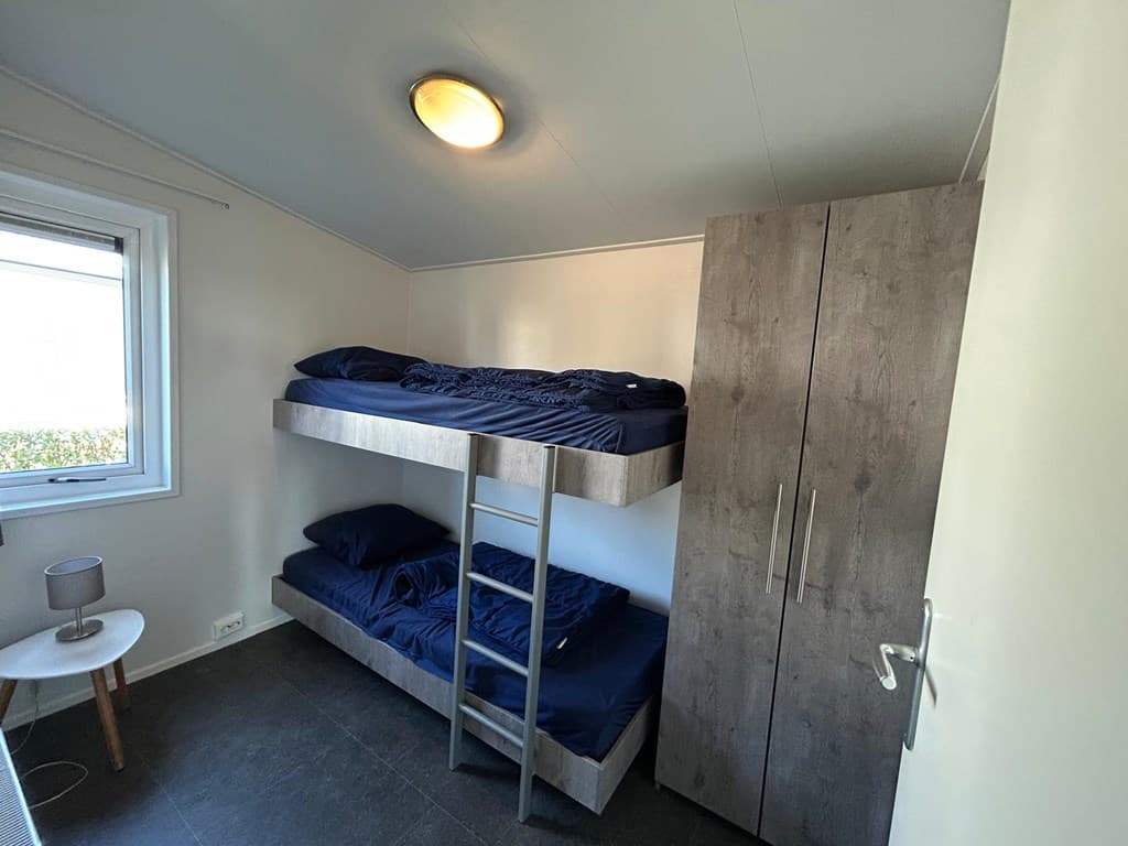 Slaapkamer met stapelbed, kast en een raam dat uitkijkt op de buitenomgeving.