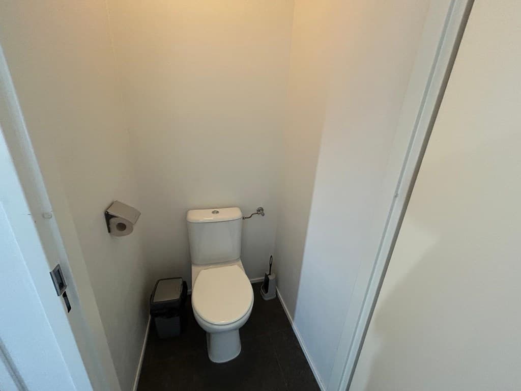 Wit toilet in een neutraal uitgevoerde toiletruimte met vloerbedekking en beperkte wanddecoratie.