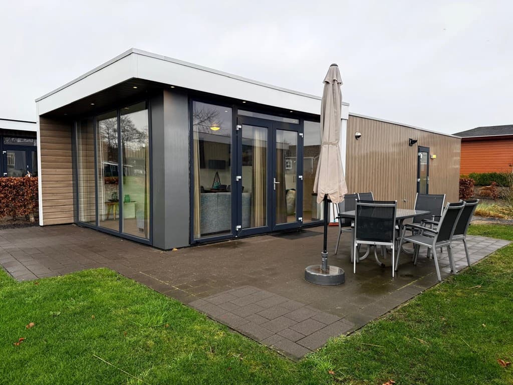 Moderne vakantiewoning met grote ramen, terras met tafel en stoelen, en parasol op EuroParcs Veluwemeer