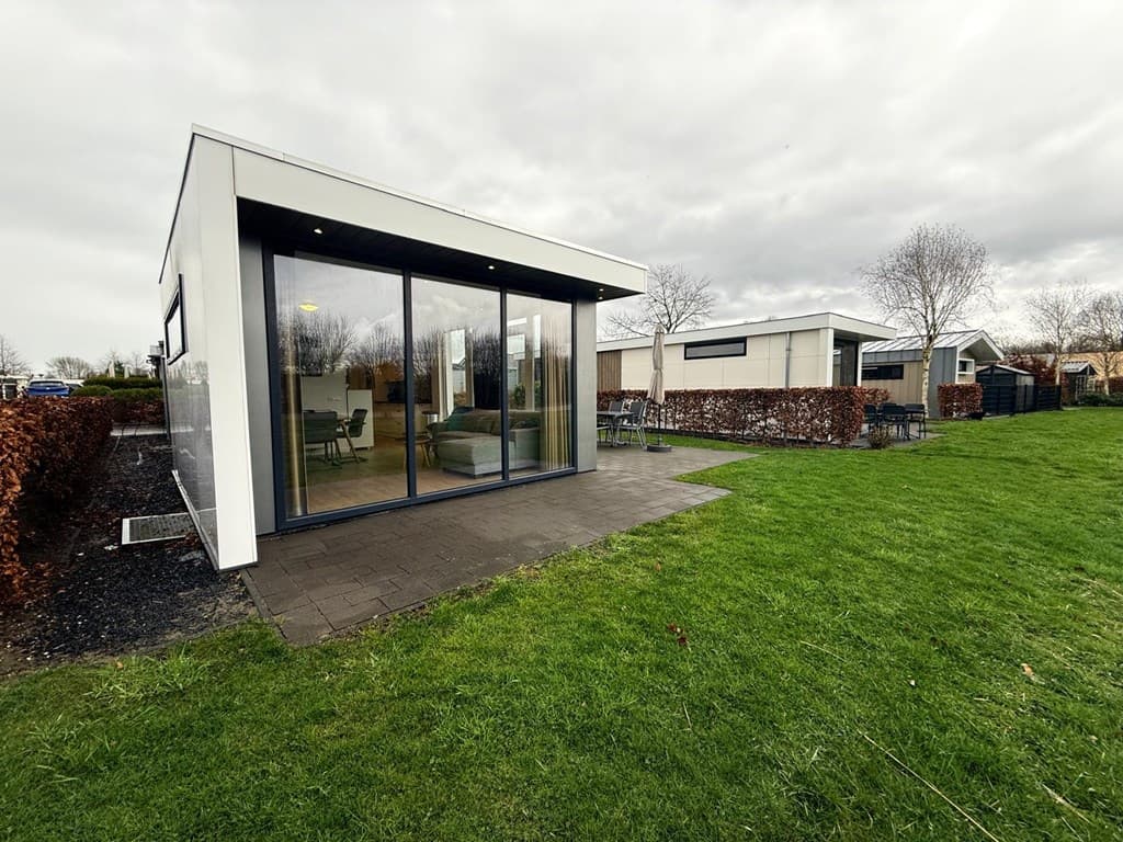 Moderne vakantiewoning met groot terras en glazen deuren, omringd door gras en borders met struiken.