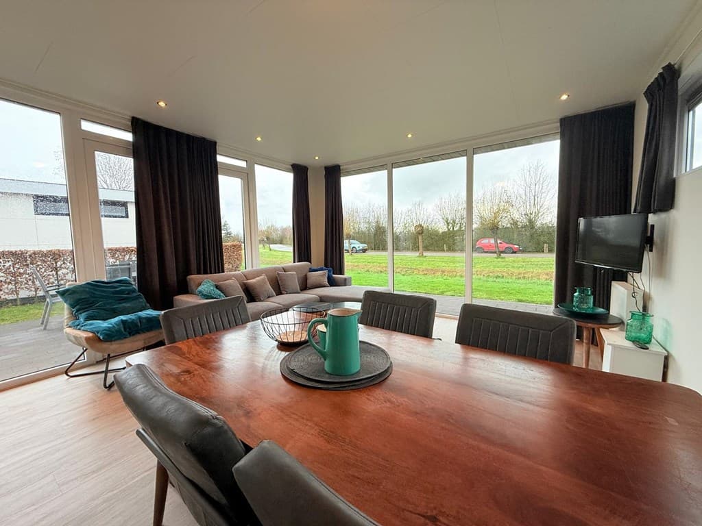Lichte woonkamer met grote ramen, een houten eettafel en comfortabele bank bij EuroParcs Veluwemeer.
