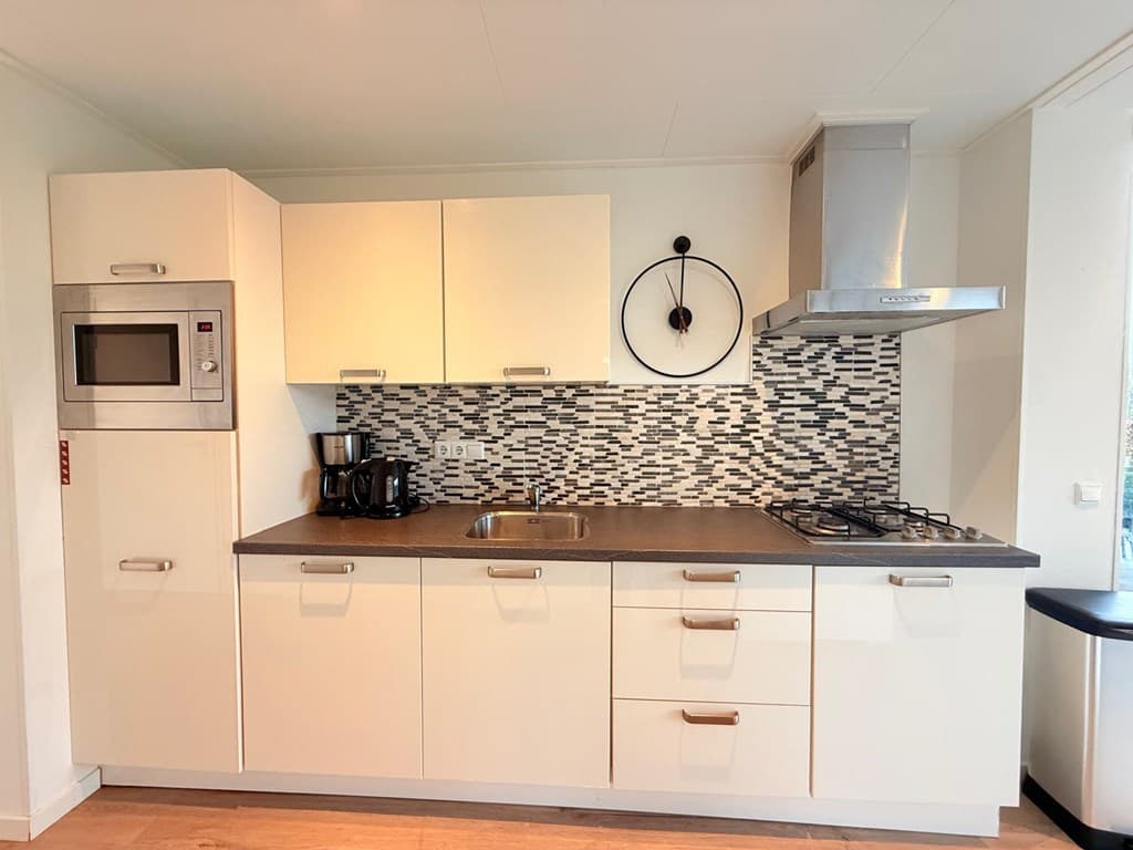 Keuken met moderne inrichting, inclusief oven, kookplaat, afzuigkap en een opvallende betegeling aan de muur
