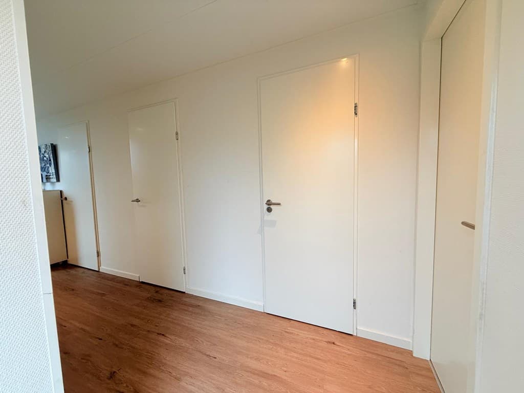 Witte muren en houten vloer met meerdere deuren in een gang van de woning