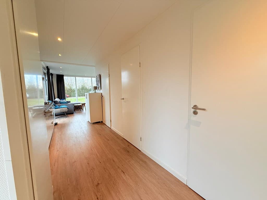 Het interieur van een woning met een lange gang die leidt naar een open woonkamer met grote ramen en een zithoek.