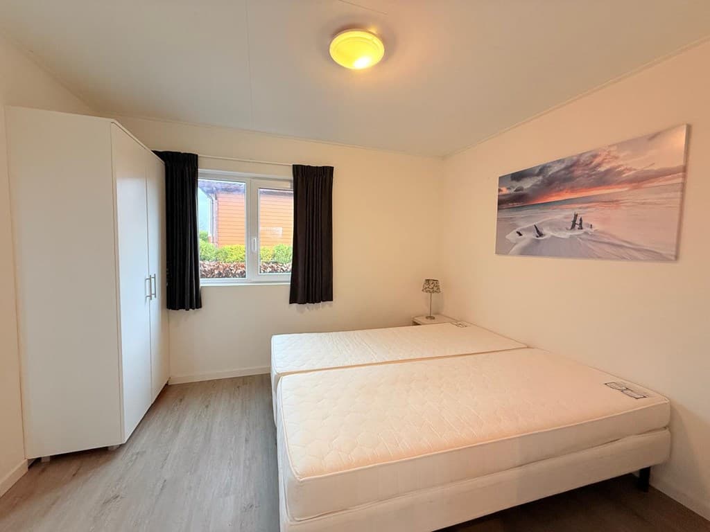Slaapkamer met twee losse bedden, een kledingkast en een raam met zicht op de buitenruimte.
