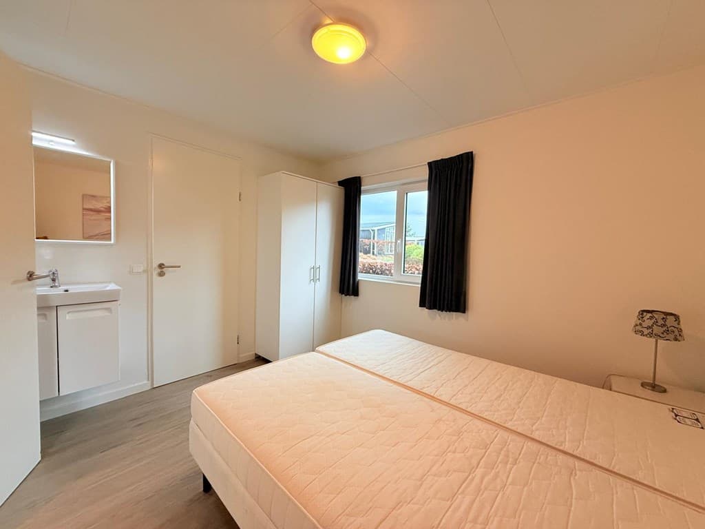 Slaapkamer met twee éénpersoonsbedden, kast, tafel met lamp en raam met verduisterende gordijnen.