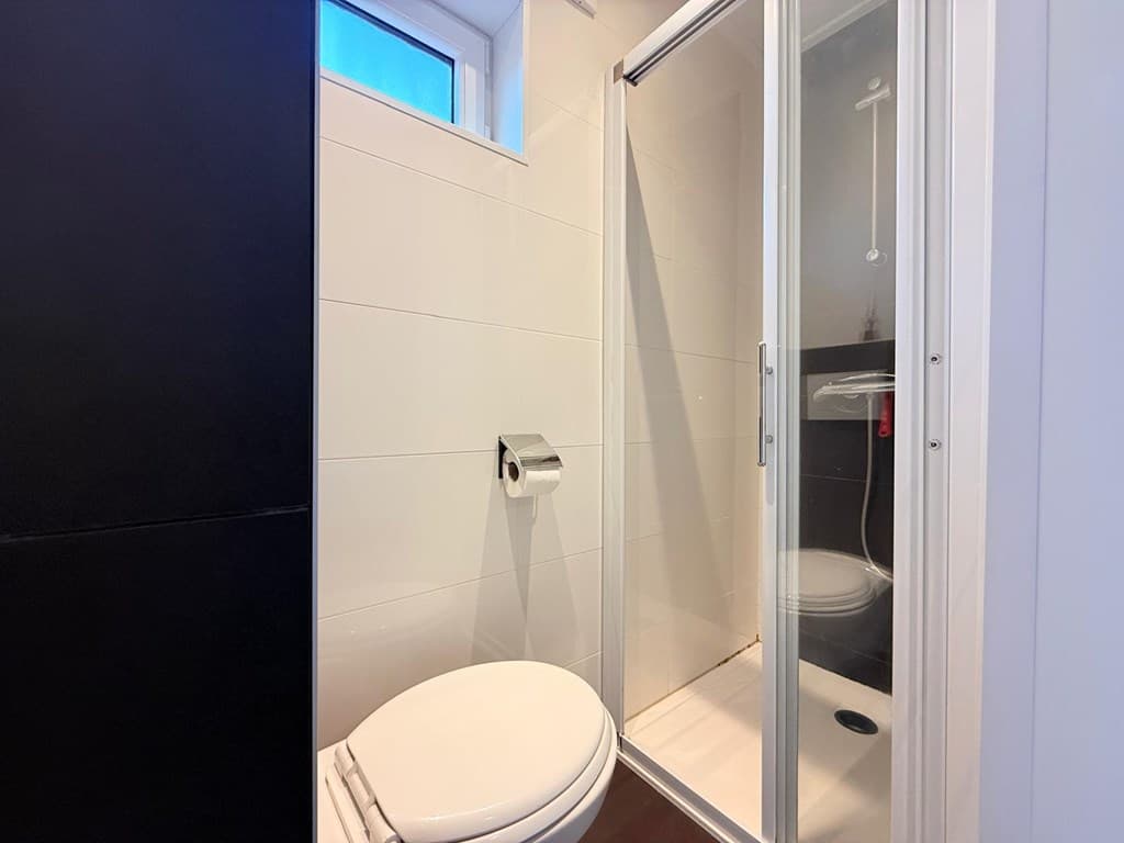 Badkamer met douchecabine, toilet en wastafel, voorzien van witte tegels en een helder raam voor natuurlijk licht