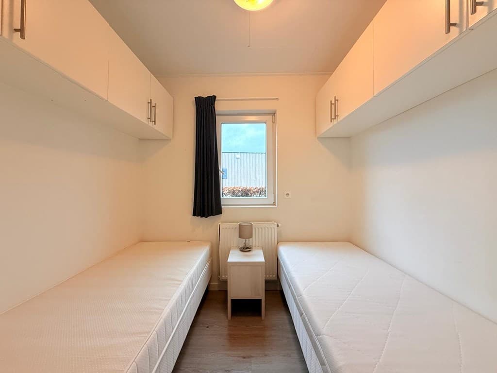 Slaapkamer met twee eenpersoonsbedden, wandkasten en een raam met uitzicht naar buiten.