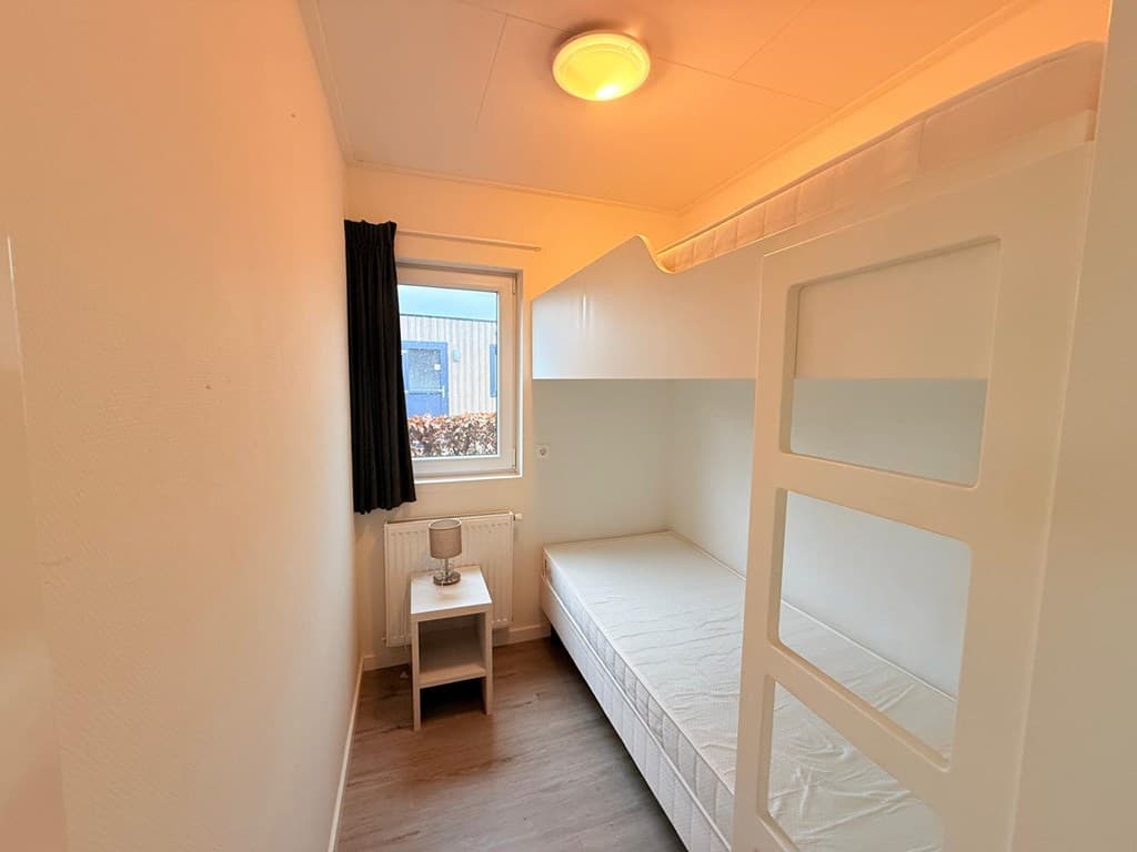 Slaapkamer met stapelbed, raam met uitzicht op buiten, en eenvoudige inrichting.