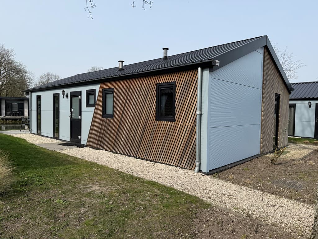 Moderne vakantiewoning met houten gevelbekleding en zwart-witte deur, gelegen in een groene omgeving.