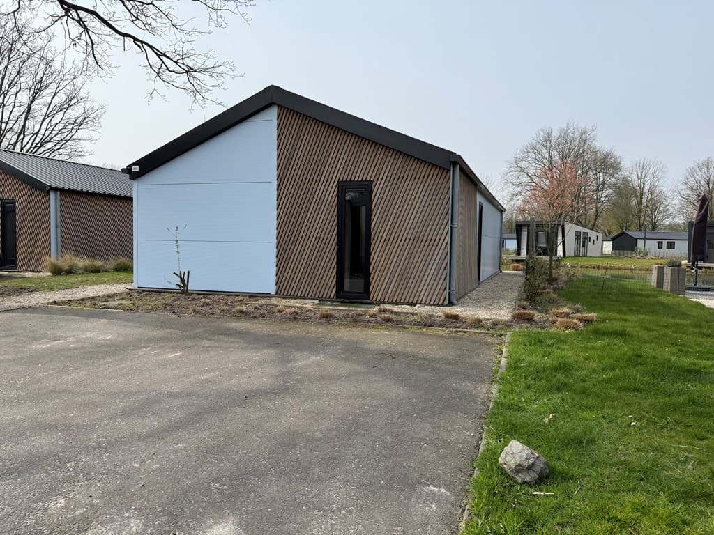 Moderne vakantiewoning met houten buitenkant en een betegeld pad in EuroParcs Kaatsheuvel, omgeven door gras en bomen