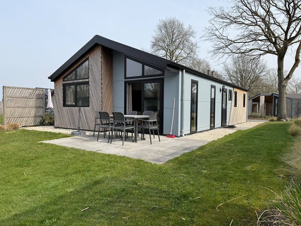 Moderne vakantiewoning met houten gevel, terras en tuinmeubilair op een groene grasveld.