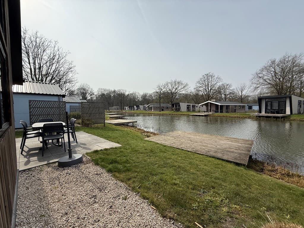 Tuin met uitzicht op het water, houten vlonder en vakantiehuizen aan de overkant, bomen op de achtergrond