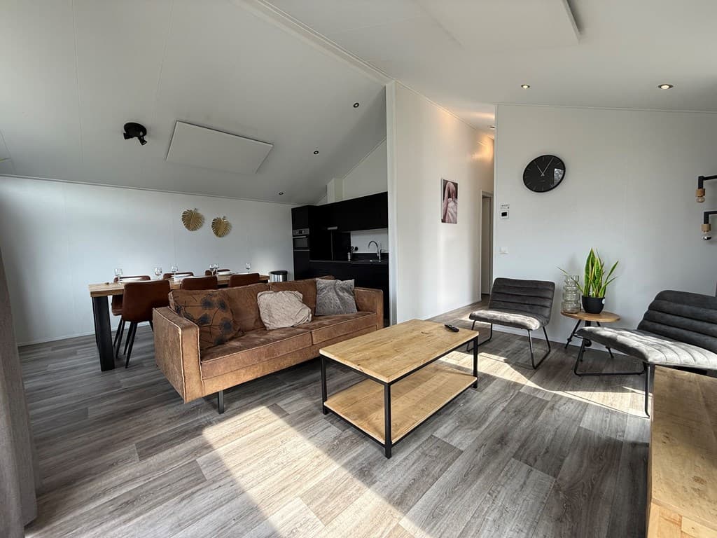 Ingerichte woonkamer met een bank, tafel, eetset en open keuken, lichte sfeer met moderne meubels en planten.
