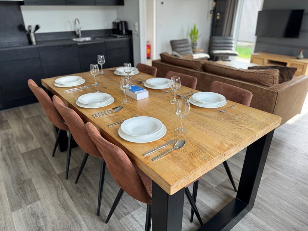 Eettafel met acht stoelen, gedekt met servies en glazen, in een modern interieur met een open keuken en zithoek