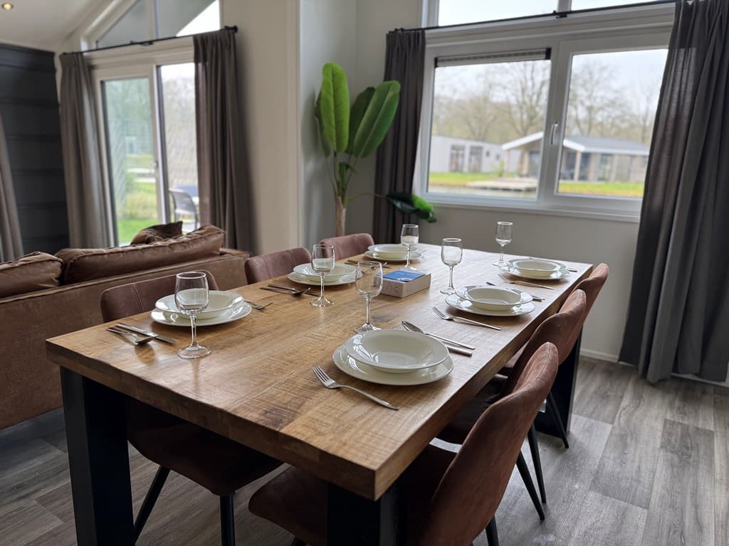 Eetkamer met een houten tafel en stoelen, gedekt voor zes personen met een uitzicht op de buitenruimte en planten.