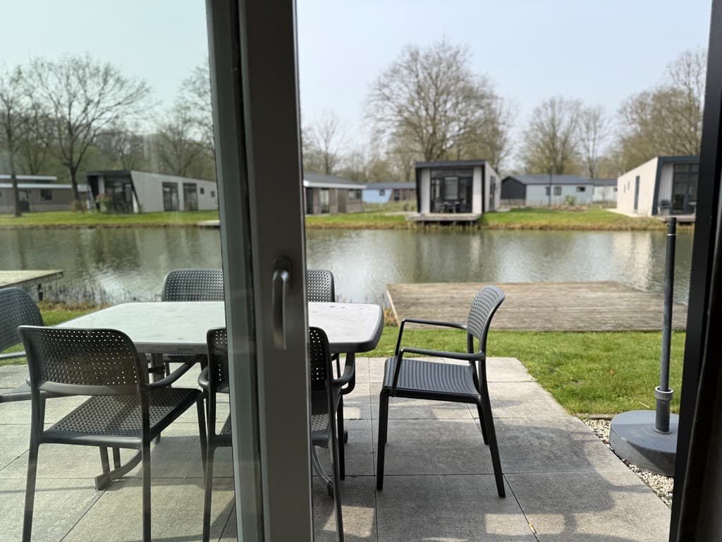 Tuin met tafel en stoelen met uitzicht op een vijver en vakantiewoningen aan de andere zijde.