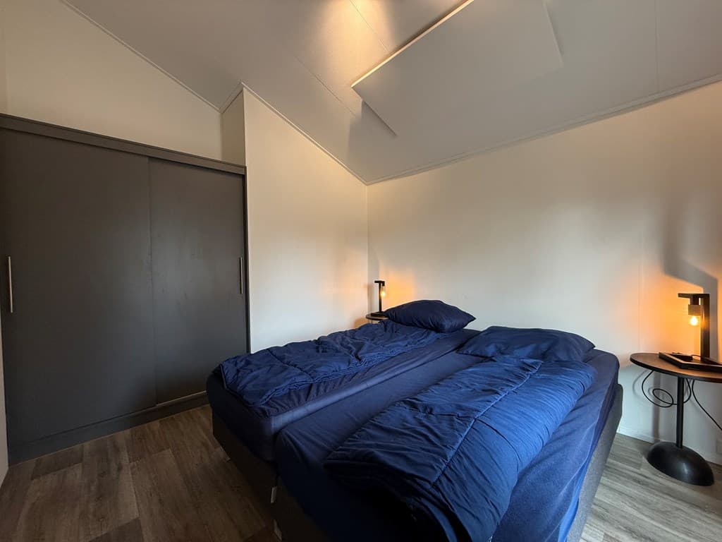 Slaapkamer met twee eenpersoonsbedden, een nachttafel en een kast met een grijze deur in een lichte ruimte