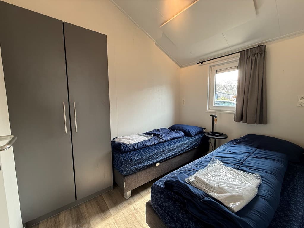 Slaapkamer met twee eenpersoonsbedden, een kast en een raam met gordijnen.